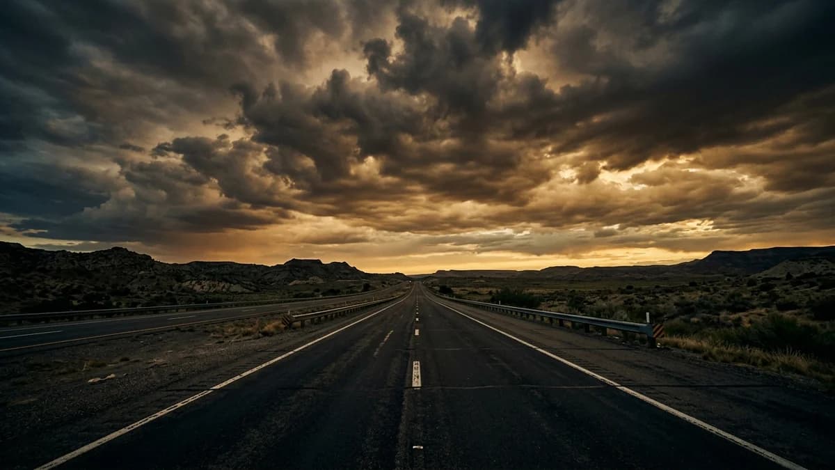 Wide empty highway stretching to the horizon under a dramatic cloudy sky, cinematic muted tones